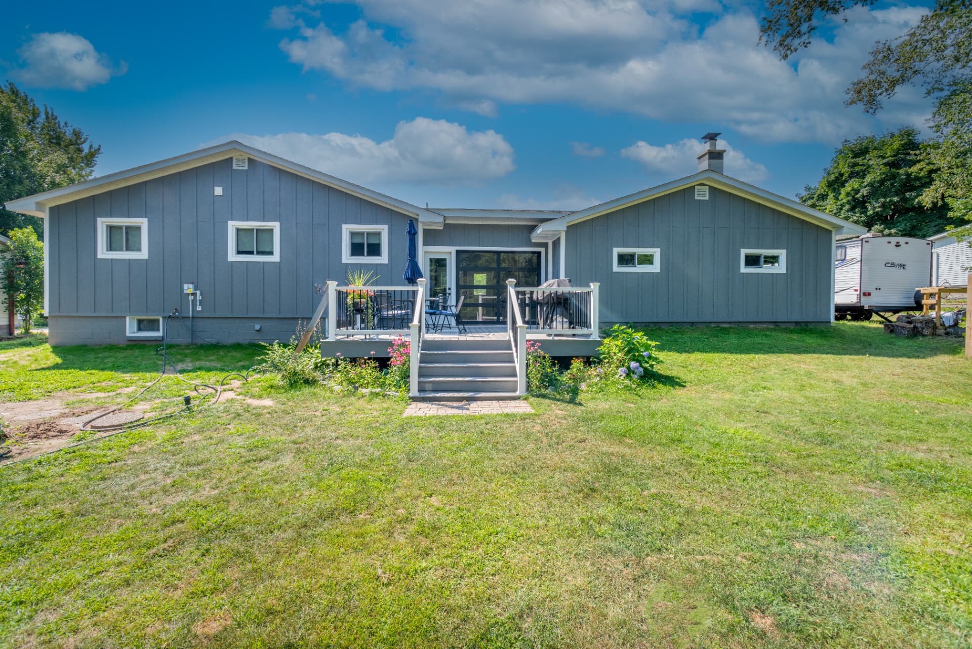 Wide rear view showing twin gable roof and raised deck with white railing on a Marquette siding remodel