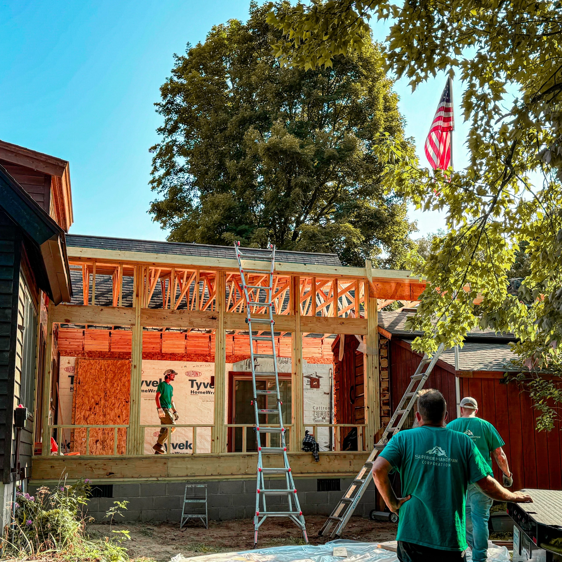 Superior Building Solutions crew framing a room addition with exposed roof trusses and Tyvek housewrap in Marquette, Michigan