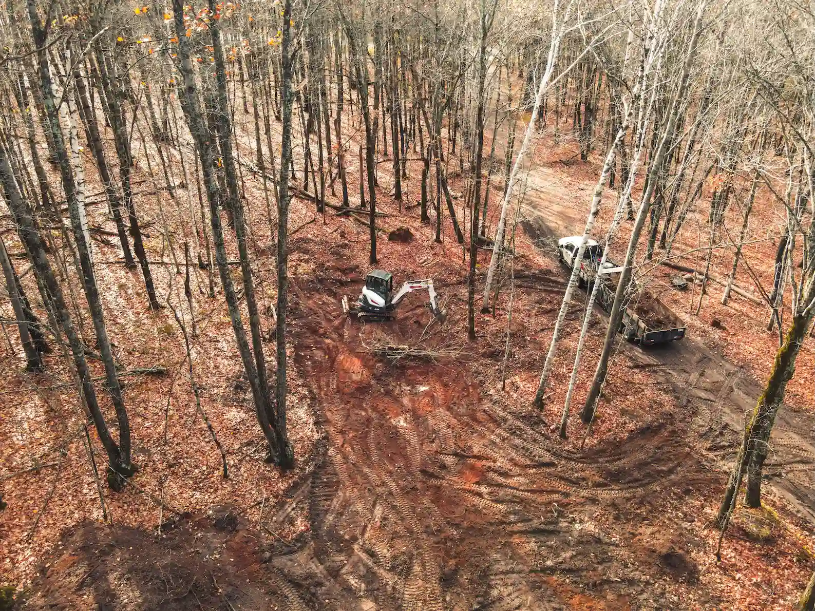 Aerial view of excavator clearing wooded lot with red clay soil in Marquette County, Michigan