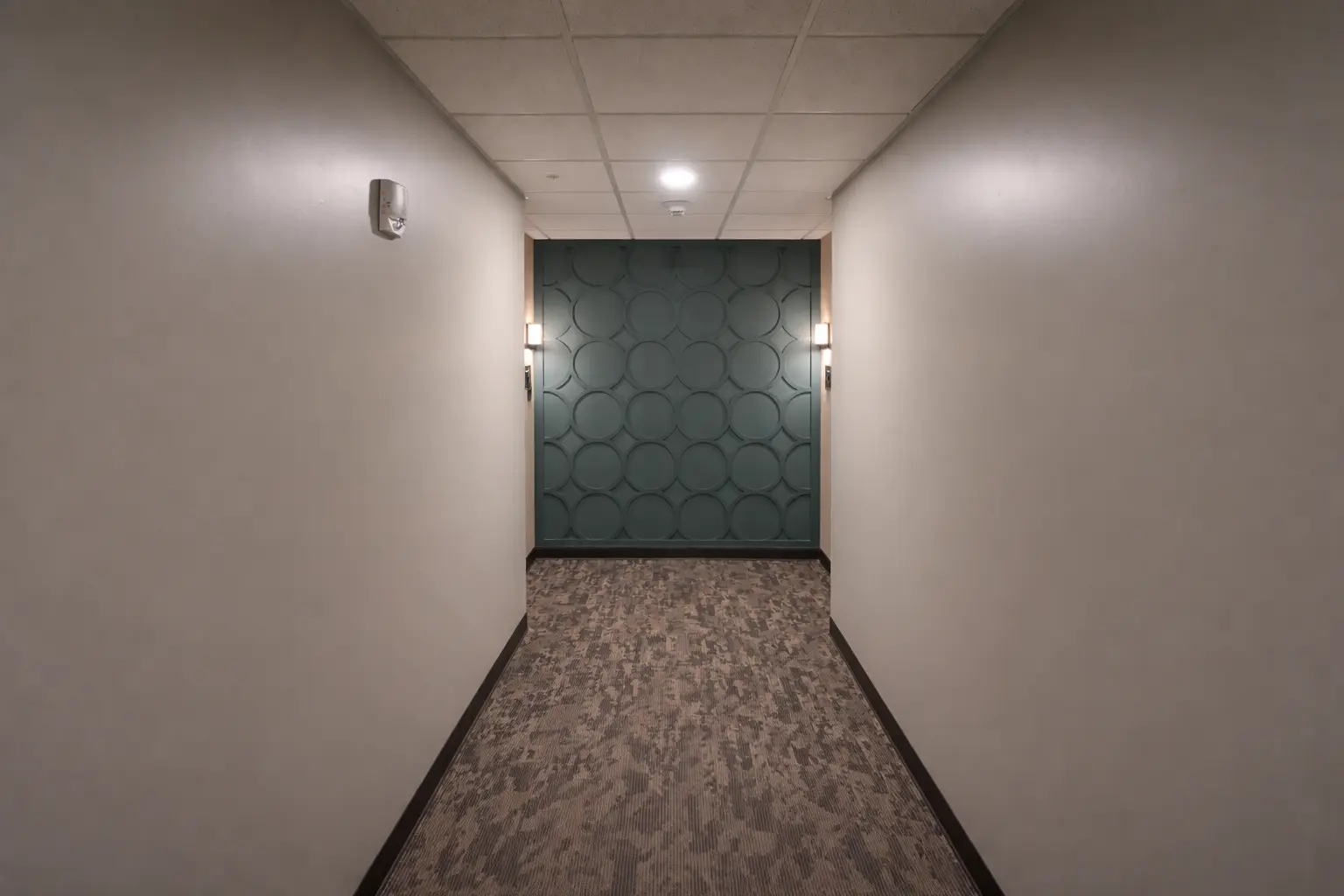Renovated commercial hallway with teal accent wall, modern sconces, and patterned carpet in Marquette, Michigan