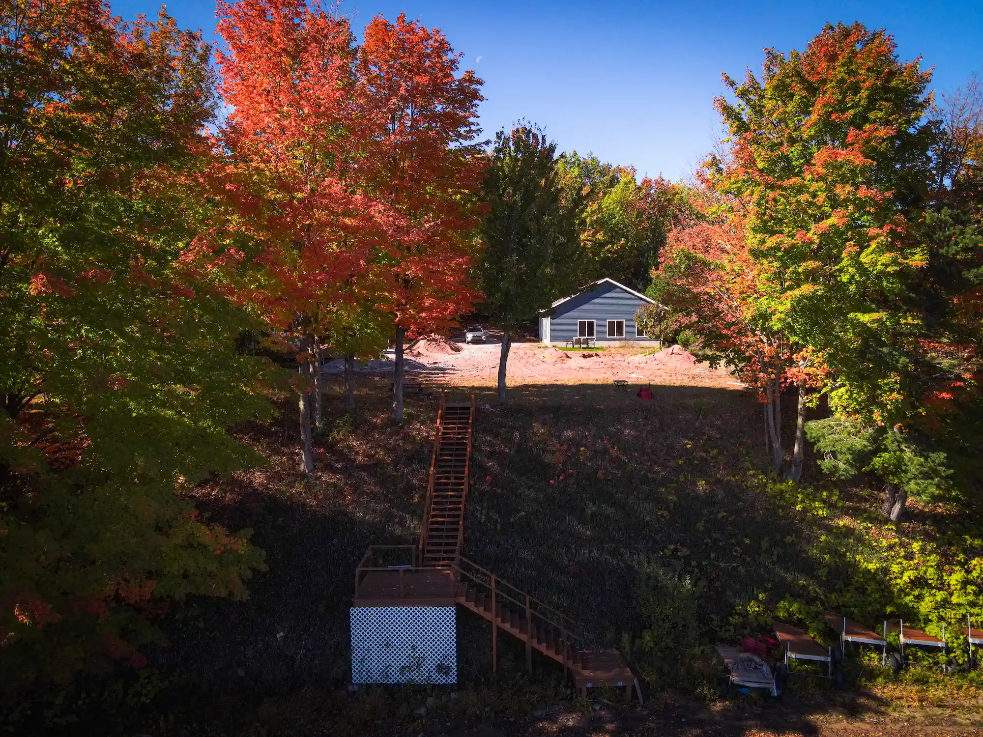 Aerial view of newly graded hillside property with wooden staircase leading to a new home surrounded by fall foliage in Marquette, Michigan