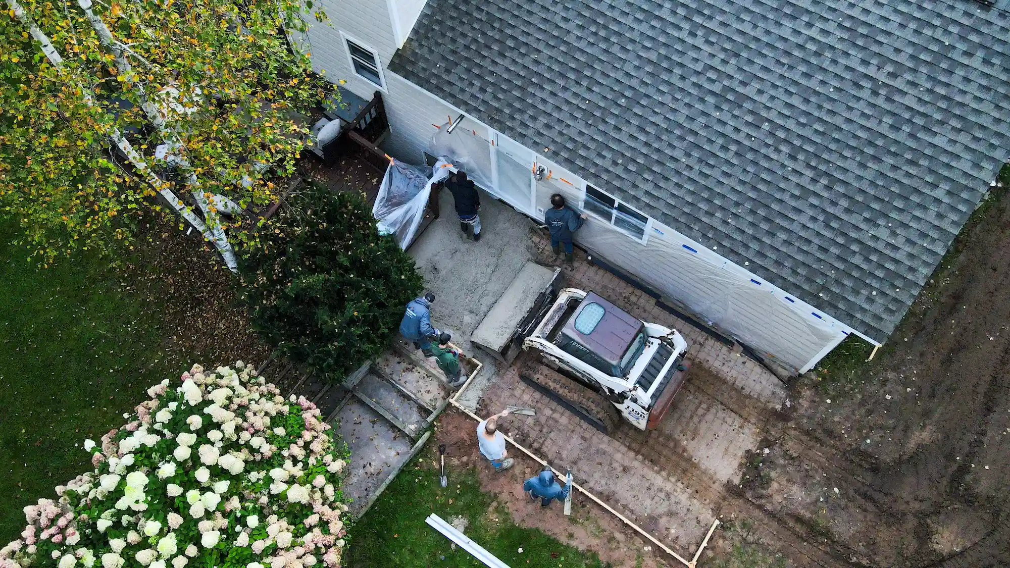 Aerial view of crew forming and excavating a patio foundation next to a white home with hydrangea bushes in Marquette, Michigan