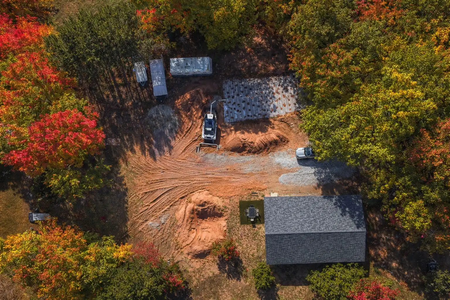 Aerial view of residential property with excavation equipment and septic system components surrounded by colorful fall trees in Marquette County, Michigan