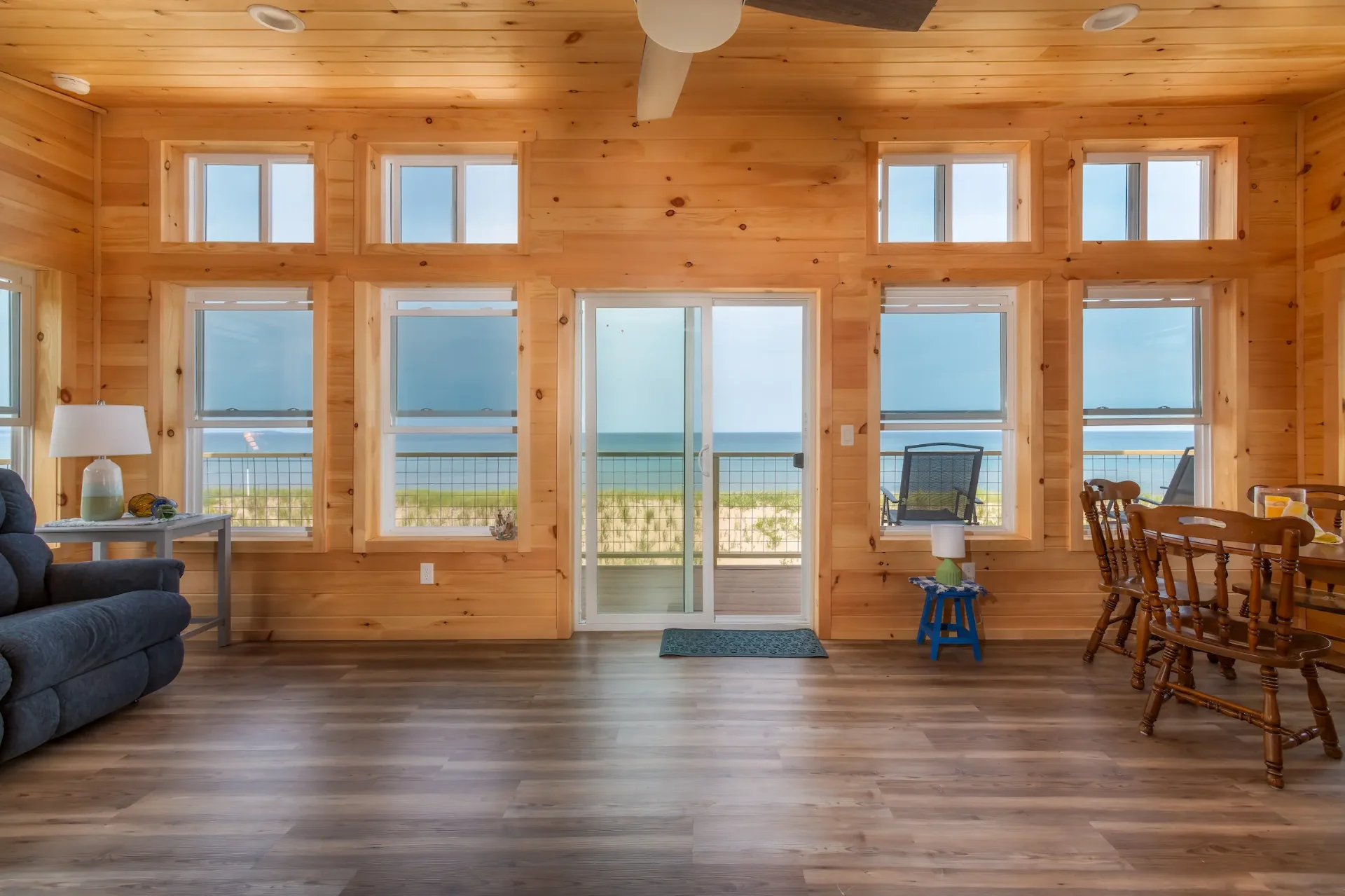 Living room with floor-to-ceiling knotty pine walls and multiple new casement windows overlooking Lake Superior in Marquette County, Michigan